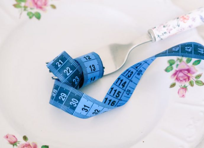 A floral plate with a fork and blue measuring tape symbolizing dieting or healthy eating.